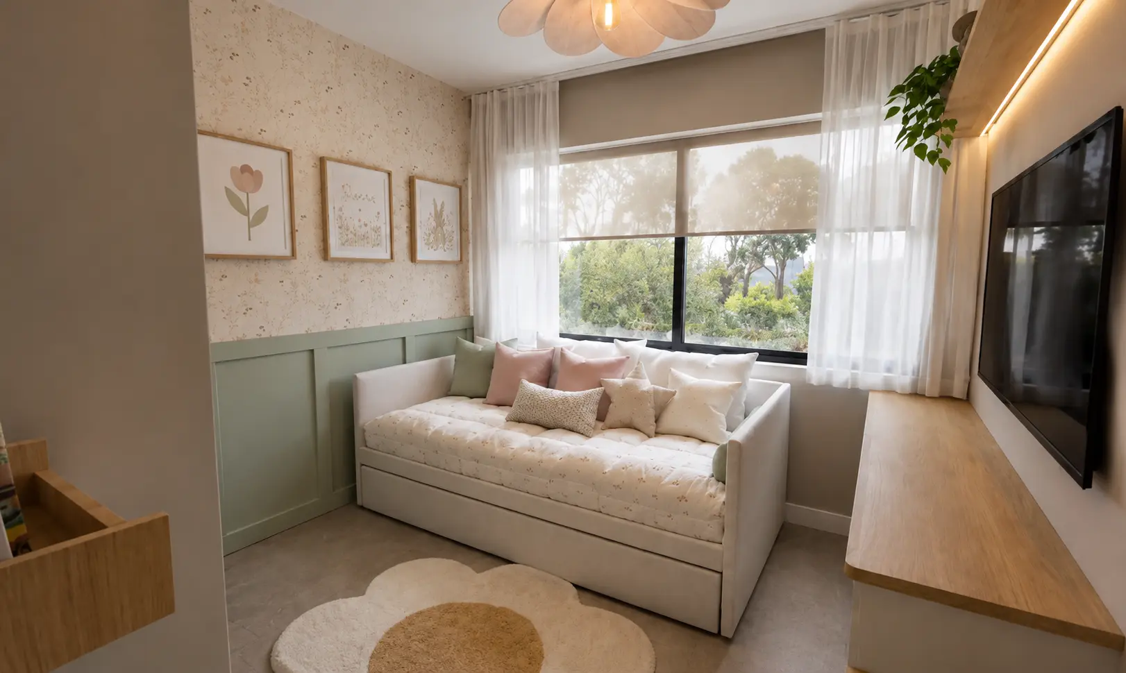 Dormitorio infantil femenino con papel tapiz floral delicado, boiserie verde salvia, sofá cama blanco con cojines rosa y crema, cuadros enmarcados, cortinas de velo y tapete en forma de flor