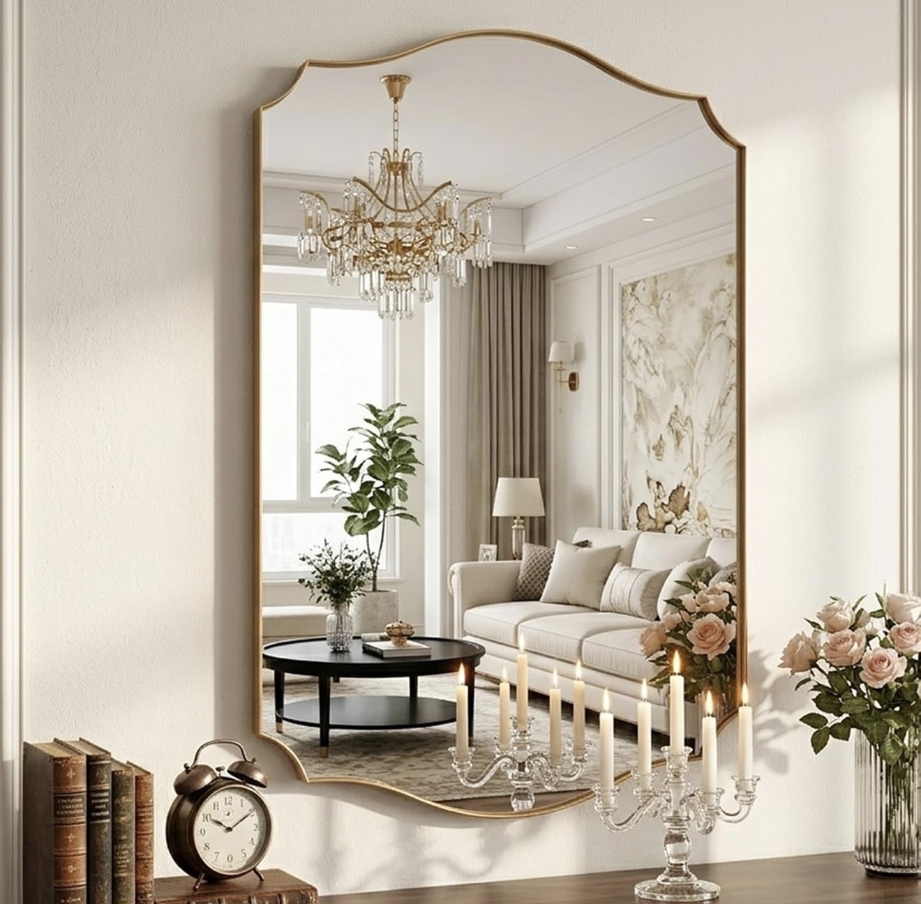 Recibidor elegante con gran espejo arqueado de marco dorado que refleja la sala, consola de madera con libros antiguos, reloj vintage, candelabro de cristal y rosas en jarrón de vidrio